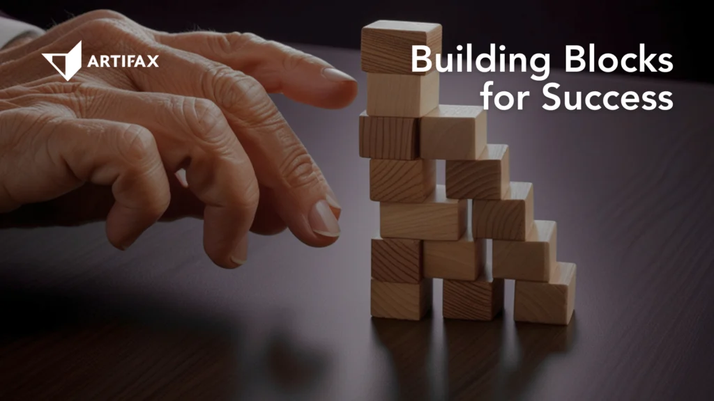 Hand arranging wooden blocks into a stacked formation on a table, with the Artifax logo and the text Building Blocks for Success.