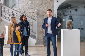 Museum guide explaining an exhibit to a family standing near a sculpture.