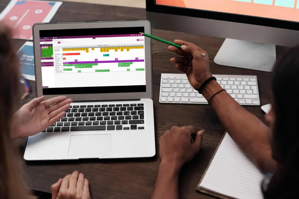 Two colleagues reviewing a colour-coded event calendar on a laptop screen.