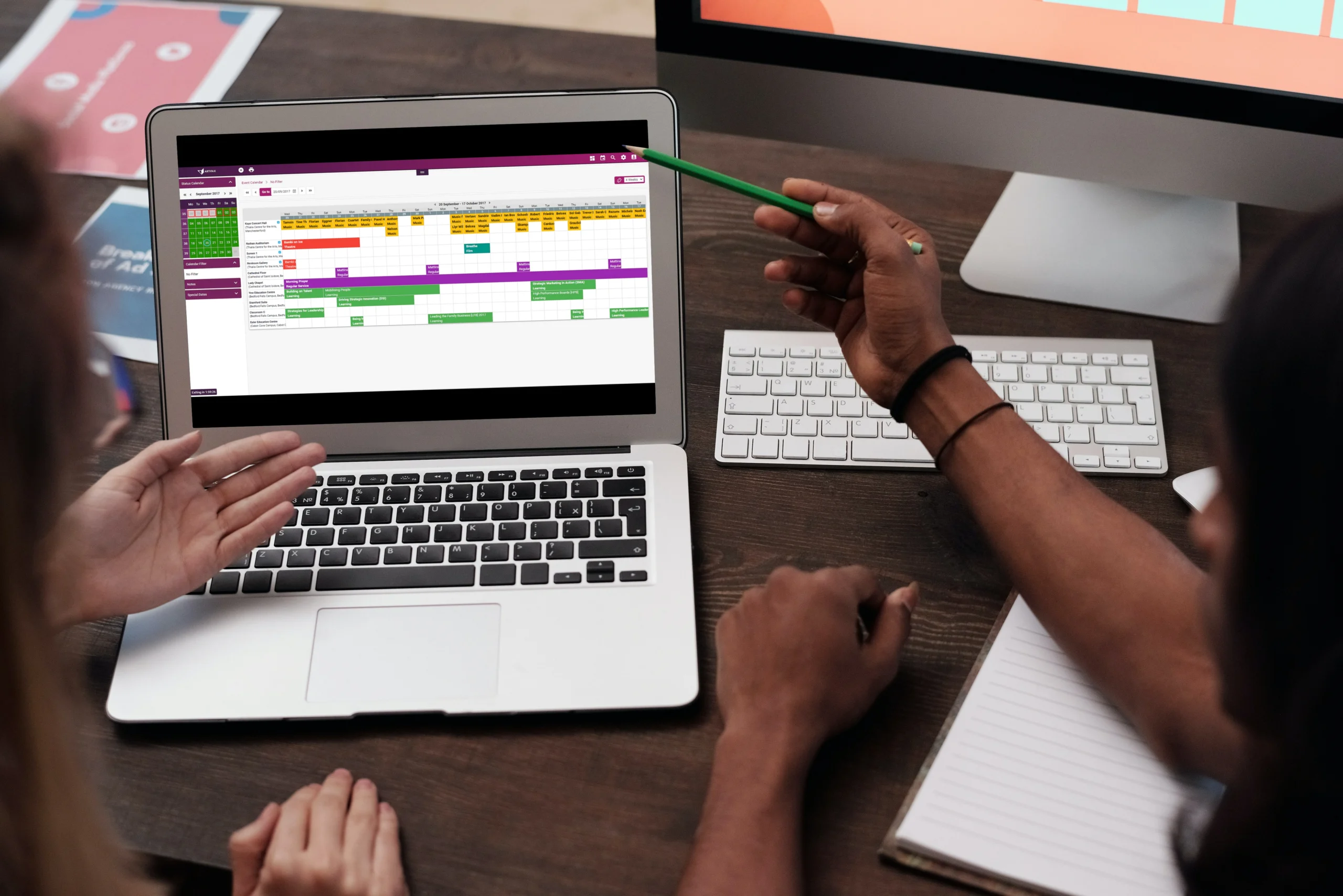 Two colleagues reviewing a colour-coded event calendar on a laptop screen.