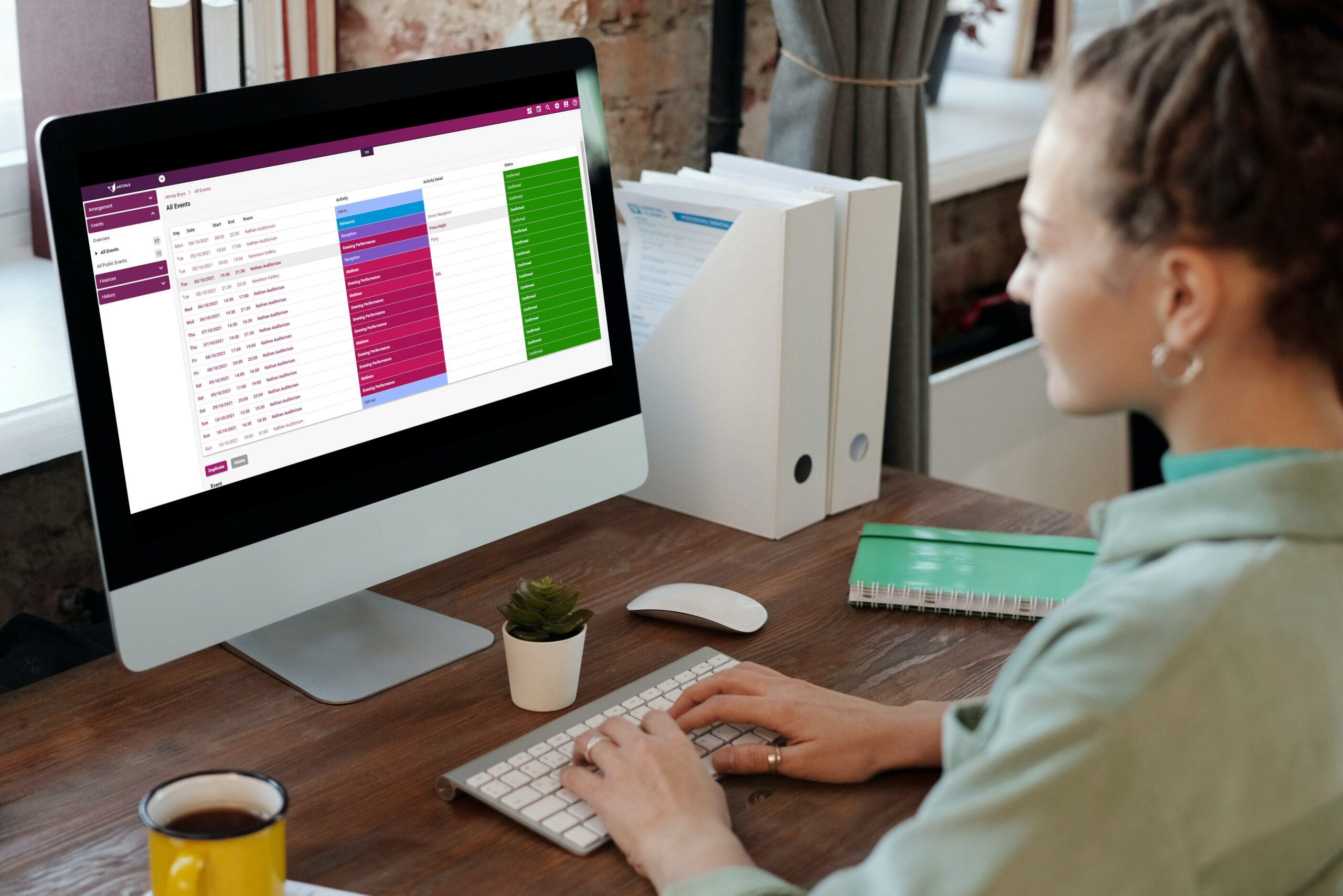 Woman working at a desktop computer displaying a list of events in Artifax.