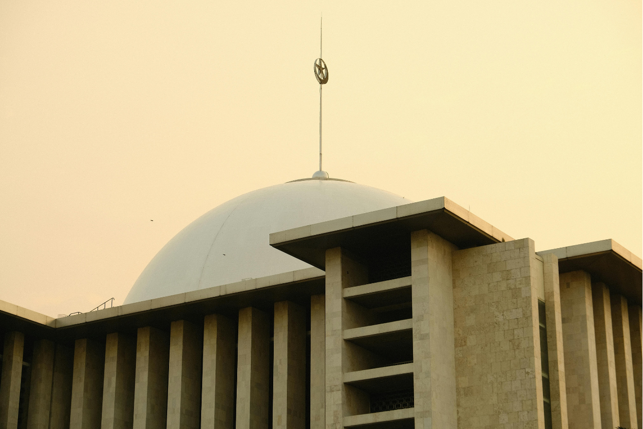 Dome of a modern mosque against a golden sky at sunset.