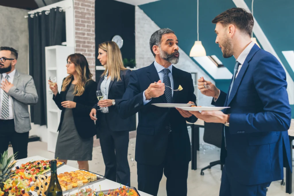 Business professionals talk and eat food at a catered networking event.