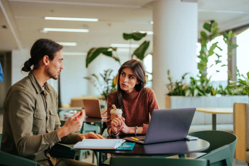 Man and woman having a serious discussion over coffee and laptops in a modern office space.