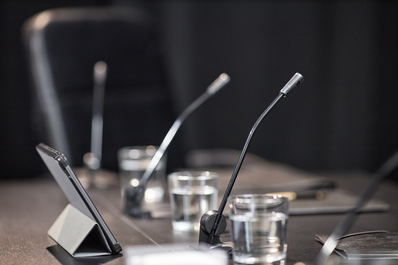 Table with multiple tabletop microphones and glasses of water.