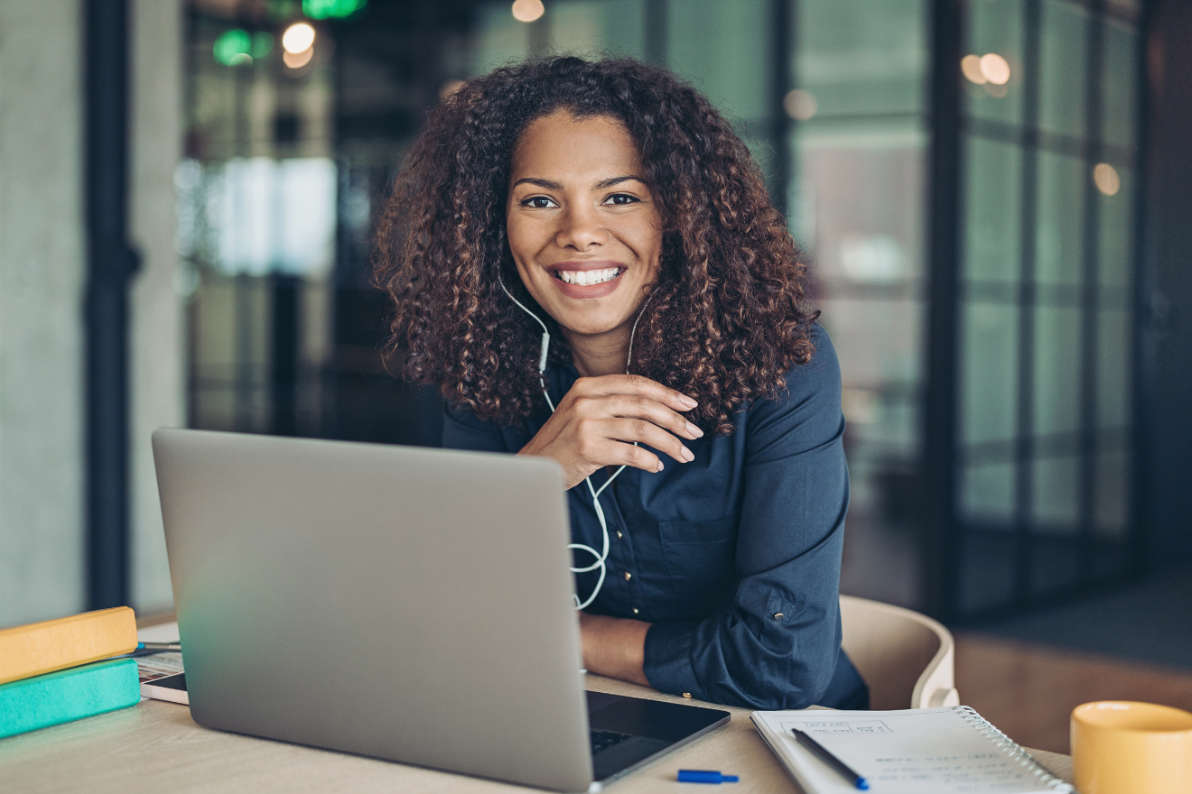 Woman smiling at laptop during a video call in a modern office.