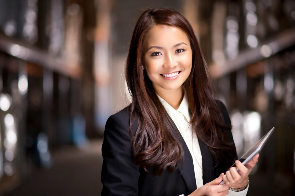 Smiling professional woman holds a tablet in a warehouse aisle.