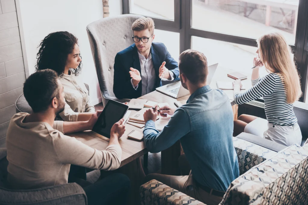 Business professionals engaged in a serious team discussion at a round table in a sunlit office.