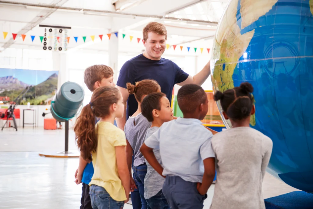 Young children listening to a guide while exploring a large globe in a science museum.