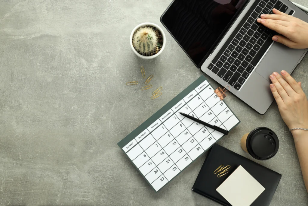 Laptop, monthly calendar, and coffee on a minimalist desk.