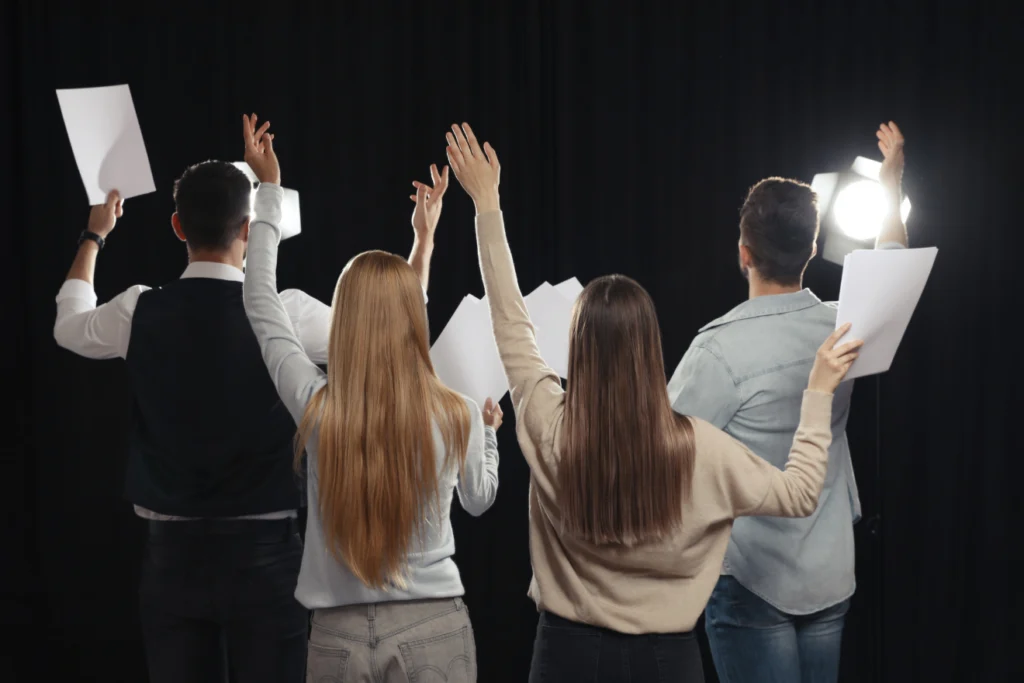 Group of performers rehearsing with scripts under stage lights.