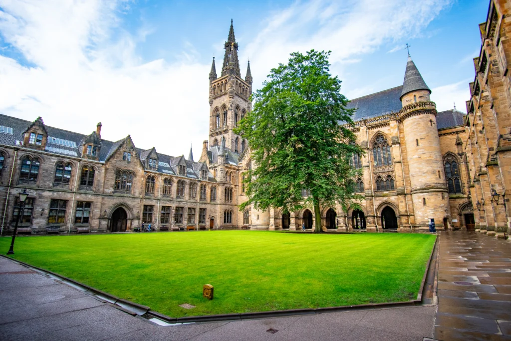 Historic university buildings surrounding a green courtyard under a bright sky.