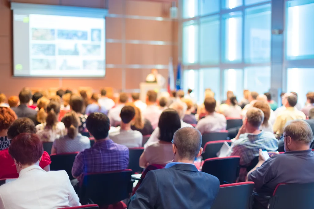 Conference attendees watching a speaker and presentation slides.
