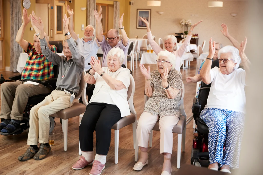 Seniors clapping and raising their hands during a seated group exercise session.
