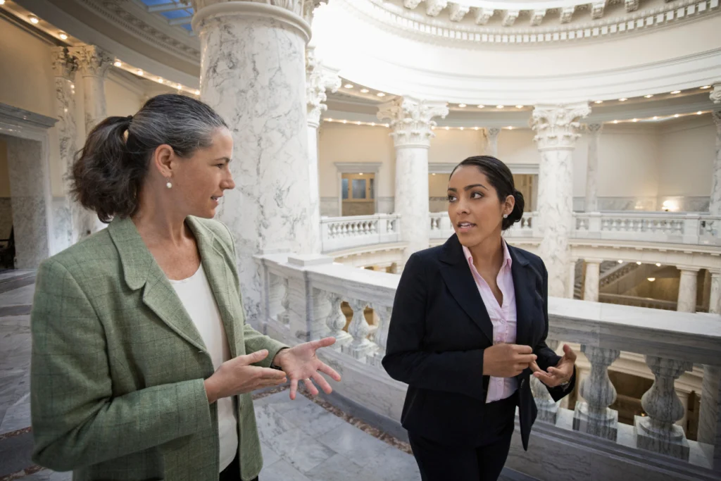 Two professionals in formal attire discussing inside a marble civic building.