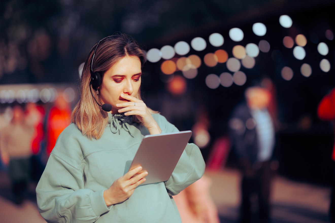 Event staff member wearing a headset reviews information on a tablet in an outdoor setting.