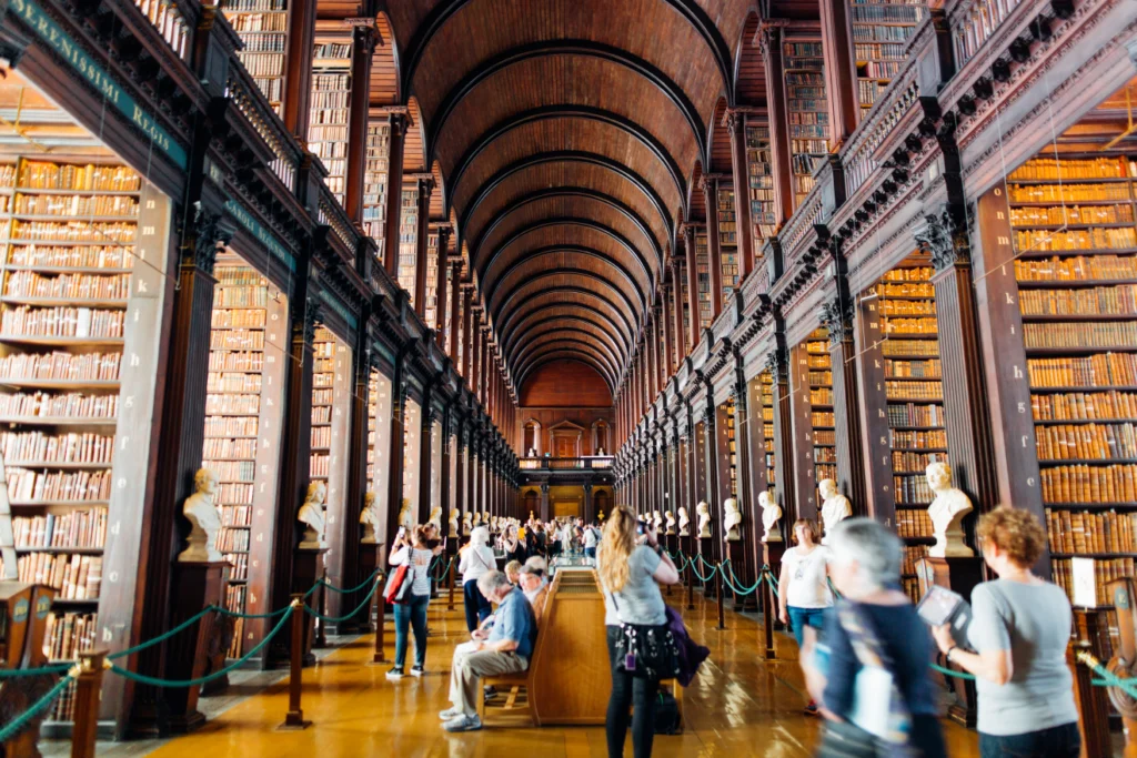 Visitors walking through a grand historic library with tall shelves and arched ceilings.