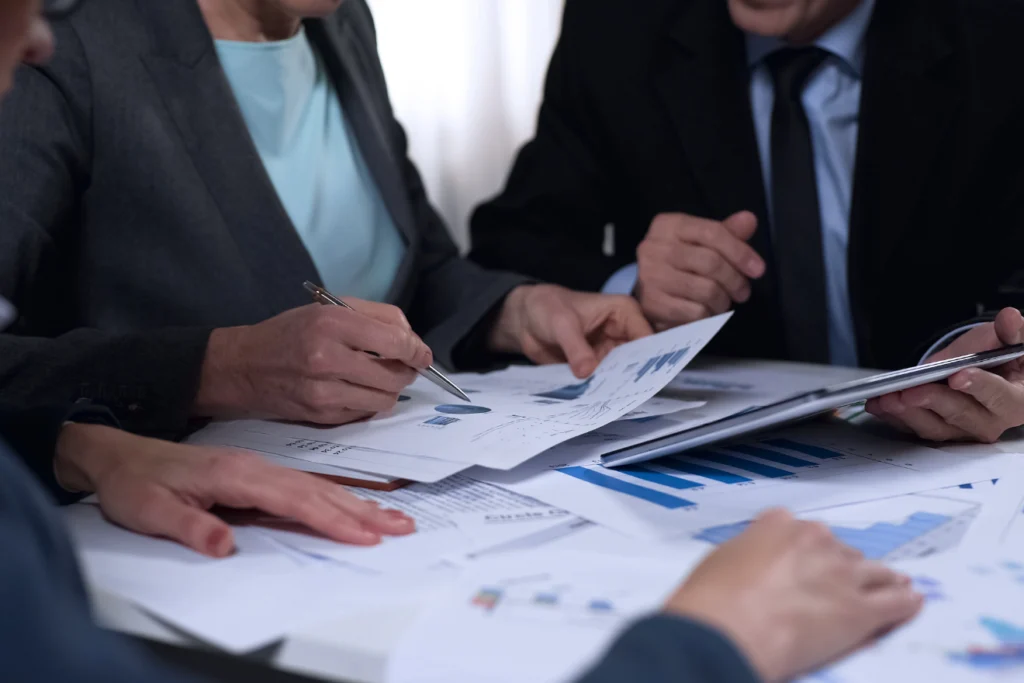 Business professionals pointing at printed reports and charts at a desk.