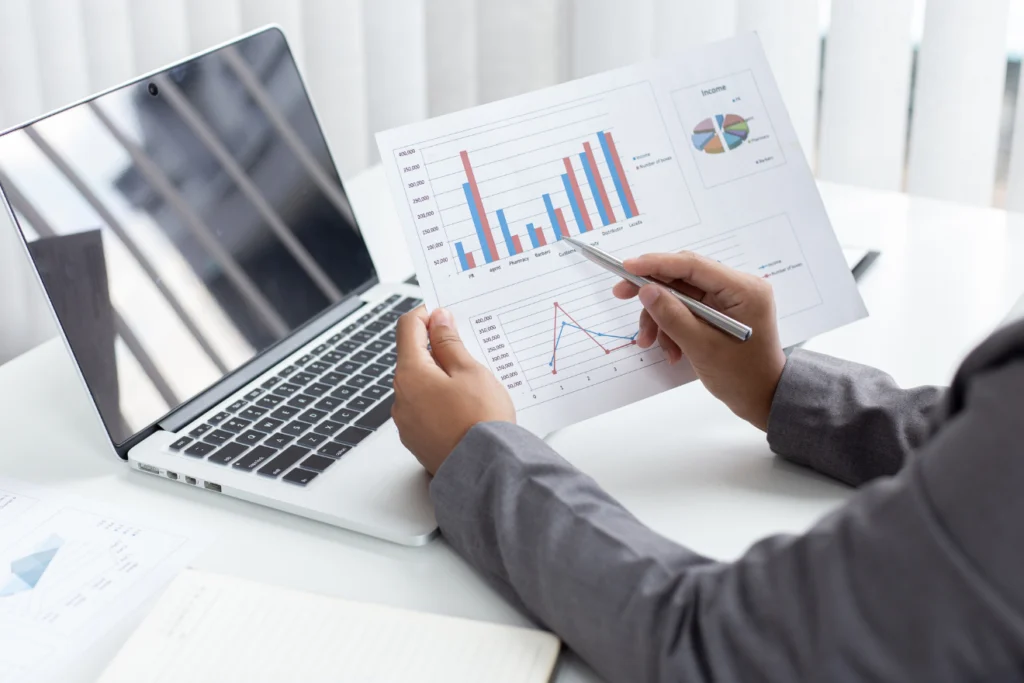 A person reviewing printed charts and graphs beside a laptop.