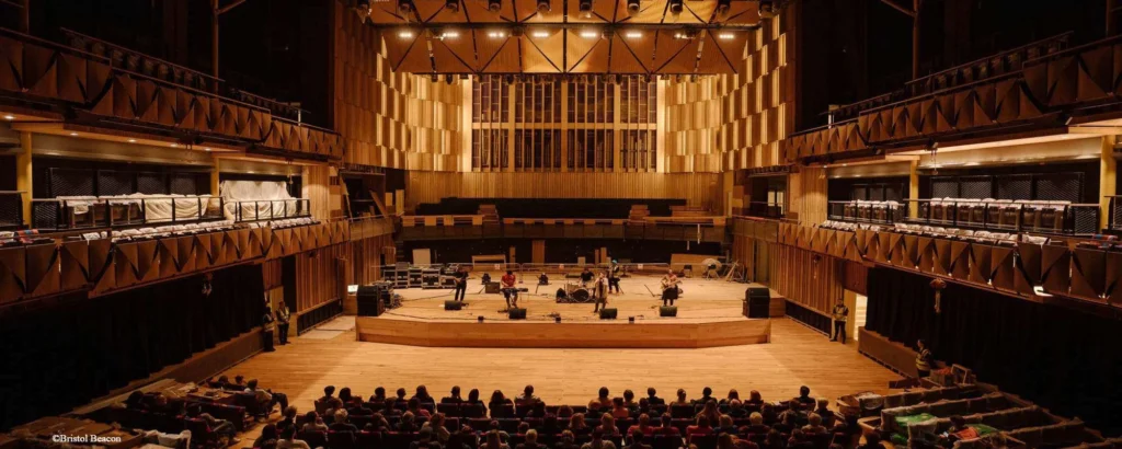 Interior of Bristol Beacon concert hall with audience seated and musicians performing on stage