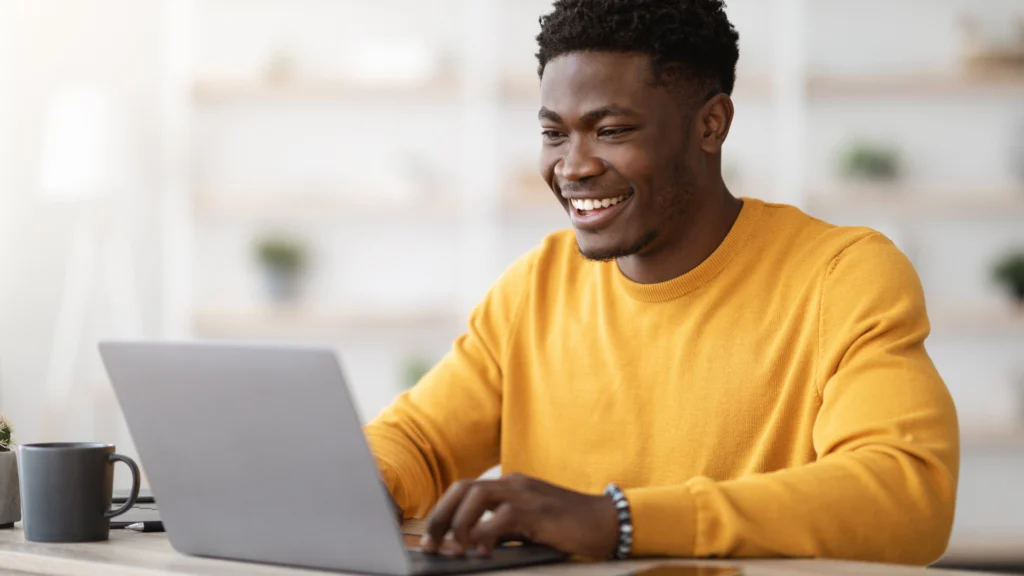 Man smiling while working on a laptop at home.