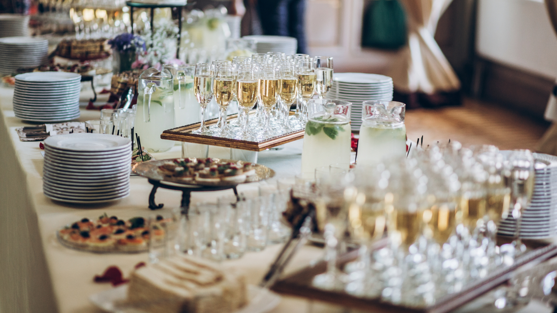 Catering table with champagne flutes, lemonade pitchers, plates, and appetizers set up for a formal event.
