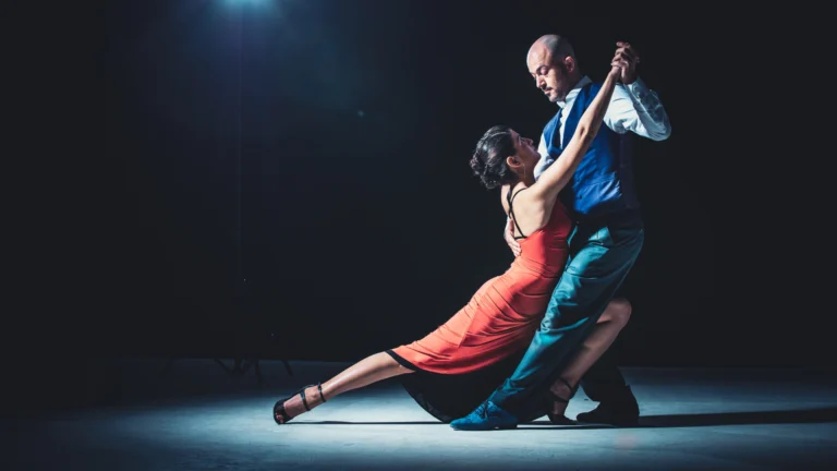 Two dancers perform a dramatic partnered dance under stage lighting, illustrating trust, balance, and the discipline developed through consistent training.