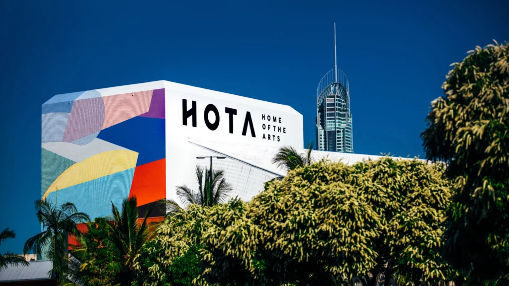 HOTA Home of the Arts building with a bold colourful mural surrounded by palm trees under a bright blue sky.