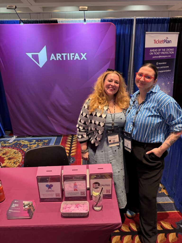 Two Artifax team members standing at the INTIX 2026 booth, with branded display, charity tokens, and TicketPlan banner in background.